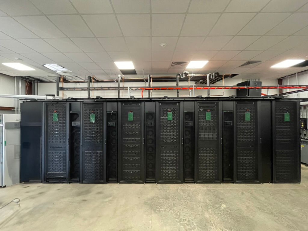 Row of black REPACSS server racks in a data center room with exposed ceiling pipes overhead